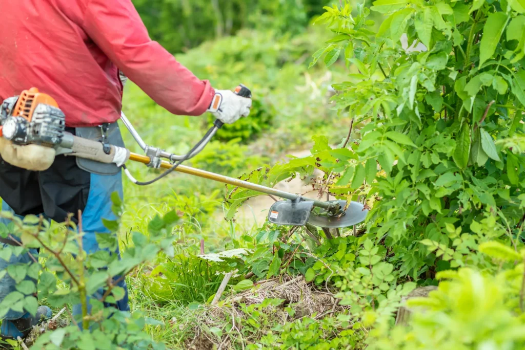草刈り機で草を刈る作業員の手元のクローズアップ