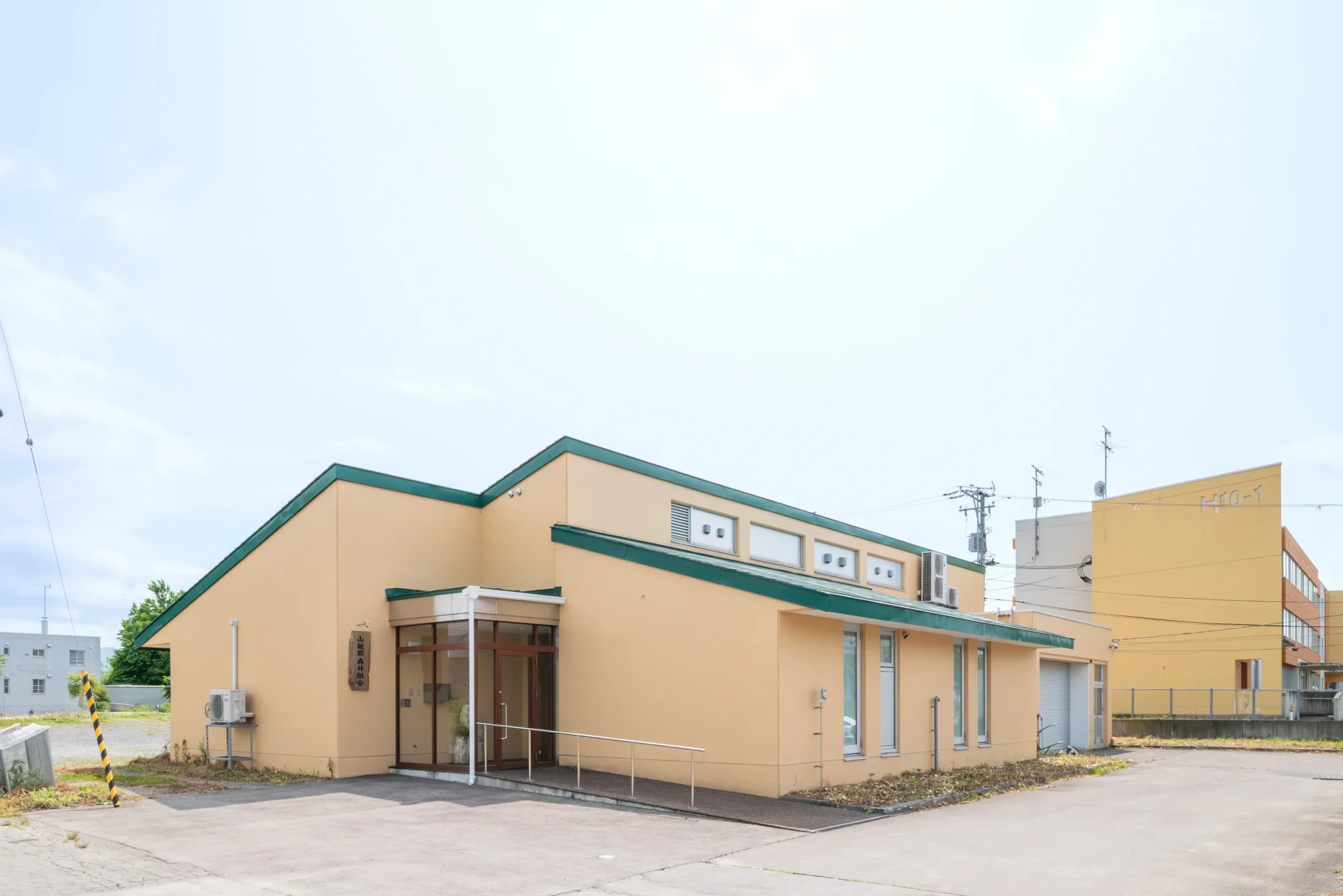 山越郡森林組合の事務所外観。クリーム色の壁と緑の屋根が特徴の建物を正面から撮影