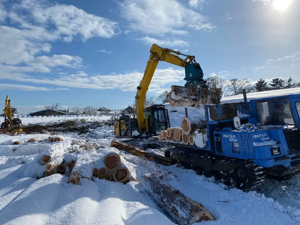 雪に覆われた現場で丸太を運搬車に積み込む林業用のローダー重機